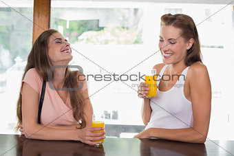 Happy female friends drinking orange juice at café