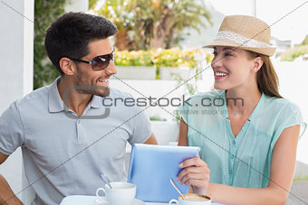 Smiling young couple using digital tablet at café