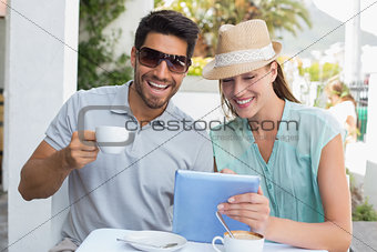 Smiling couple with coffee cup using digital tablet at café