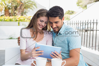 Smiling couple using digital tablet at café