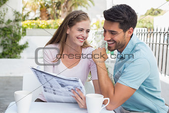 Smiling couple reading newspaper at café