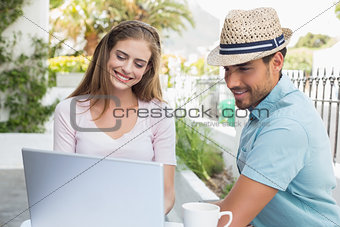 Smiling couple using laptop at café