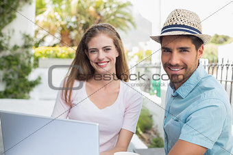 Smiling young couple using laptop at café