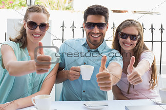 Happy friends gesturing thumbs up in café