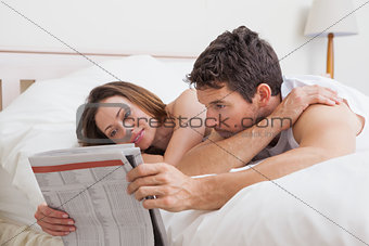 Couple reading newspaper together in bed