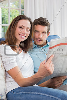 Relaxed young couple reading newspaper on couch