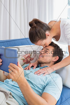Woman kissing mans forehead while he uses digital tablet