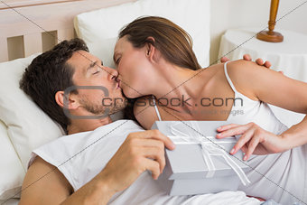 Couple kissing with gift box in hand in bed