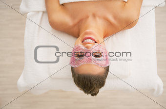 Happy young woman with eye mask laying on massage table