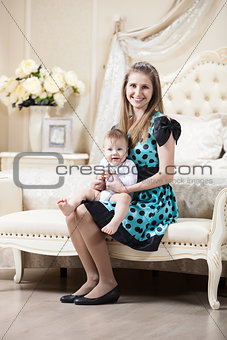 Young Caucasian woman posing with little son while sitting on couch in bedroom