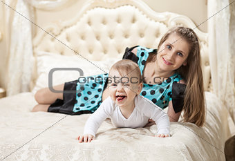 Young Caucasian mother and baby son having fun on bed at home