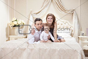 Young happy family with a baby on bed at home