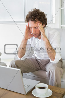 Worried man with head in hands looking at laptop at home