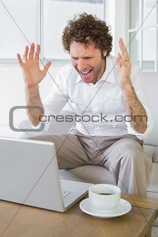 Frustrated man shouting in front of laptop at home