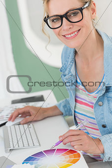 Blonde designer using a colour wheel smiling at camera