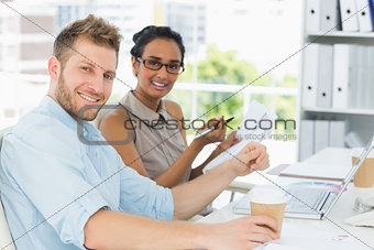 Business partners working together at desk smiling at camera