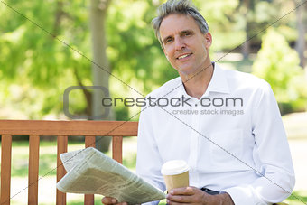 Businessman with disposable cup and newspaper in park