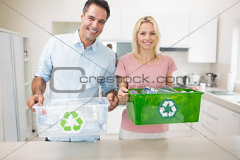 Smiling couple carrying recycling containers in kitchen