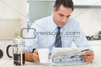 Well dressed man with coffee cup reading newspaper in kitchen