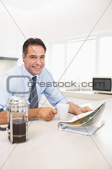 Smiling well dressed man with coffee cup and newspaper in kitchen