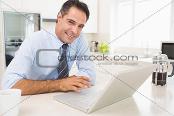 Smiling well dressed man using laptop in kitchen