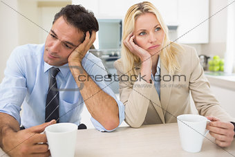 Well dressed thoughtful couple with coffee cups in kitchen