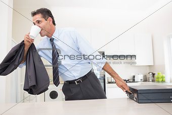 Well dressed man drinking coffee while holding briefcase in kitchen