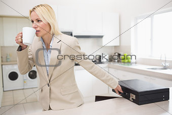 Well dressed woman drinking coffee while holding briefcase in kitchen