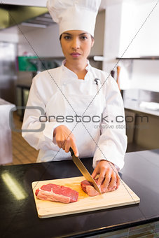 Serious female chef cutting meat in kitchen