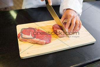 Mid section of hands cutting meat