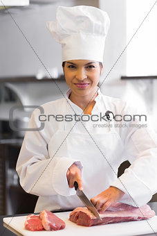 Smiling female chef cutting meat in kitchen