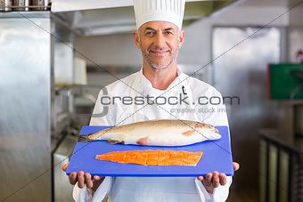 Confidence chef holding tray of raw fish in kitchen