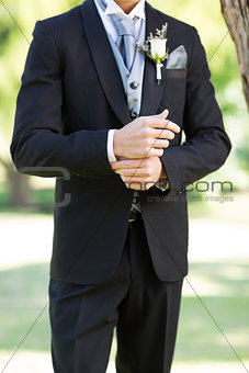 Sophisticated groom adjusting sleeve in garden
