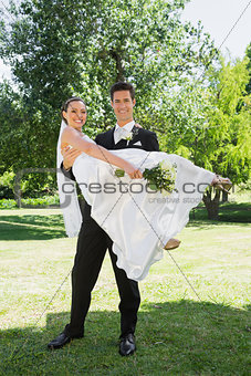 Happy groom lifting bride in arms at garden