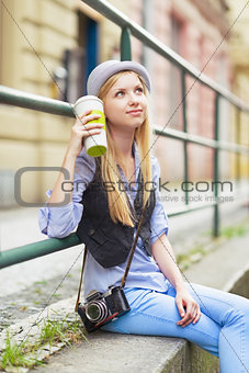 Young hipster sitting in the city with cup of hot beverage