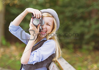 Young hipster taking photo with retro photo camera sitting on be
