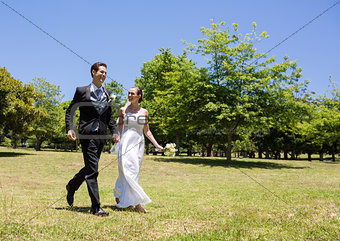 Bride and groom holding hands walking in park