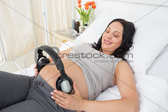 Expectant woman putting headphones on her belly