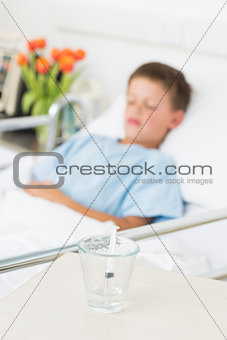 Syringe in glass with boy resting in hospital ward
