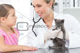 Veterinarian examining kitten with girl