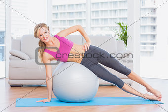 Cheerful fit blonde doing side plank with exercise ball