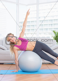 Happy fit blonde doing side plank with exercise ball