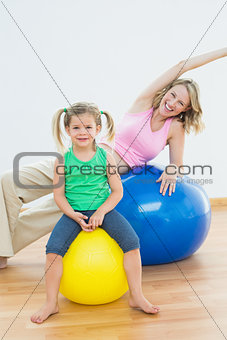 Happy pregnant woman exercising on exercise ball with young daughter