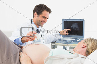 Happy doctor showing pregnant woman her baby on sonagram