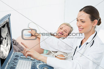 Cheerful female doctor showing woman her baby on ultrasound