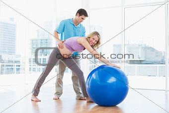 Trainer exercising with smiling pregnant client and exercise ball