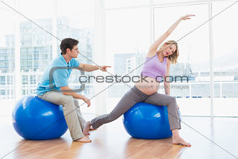 Trainer exercising with blonde pregnant client on exercise balls