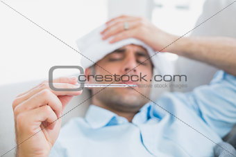 Sick man lying on sofa checking his temperature