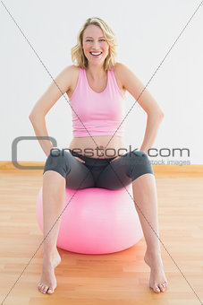 Cheerful blonde pregnant woman sitting on exercise ball