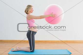 Cheerful blonde pregnant woman lifting exercise ball